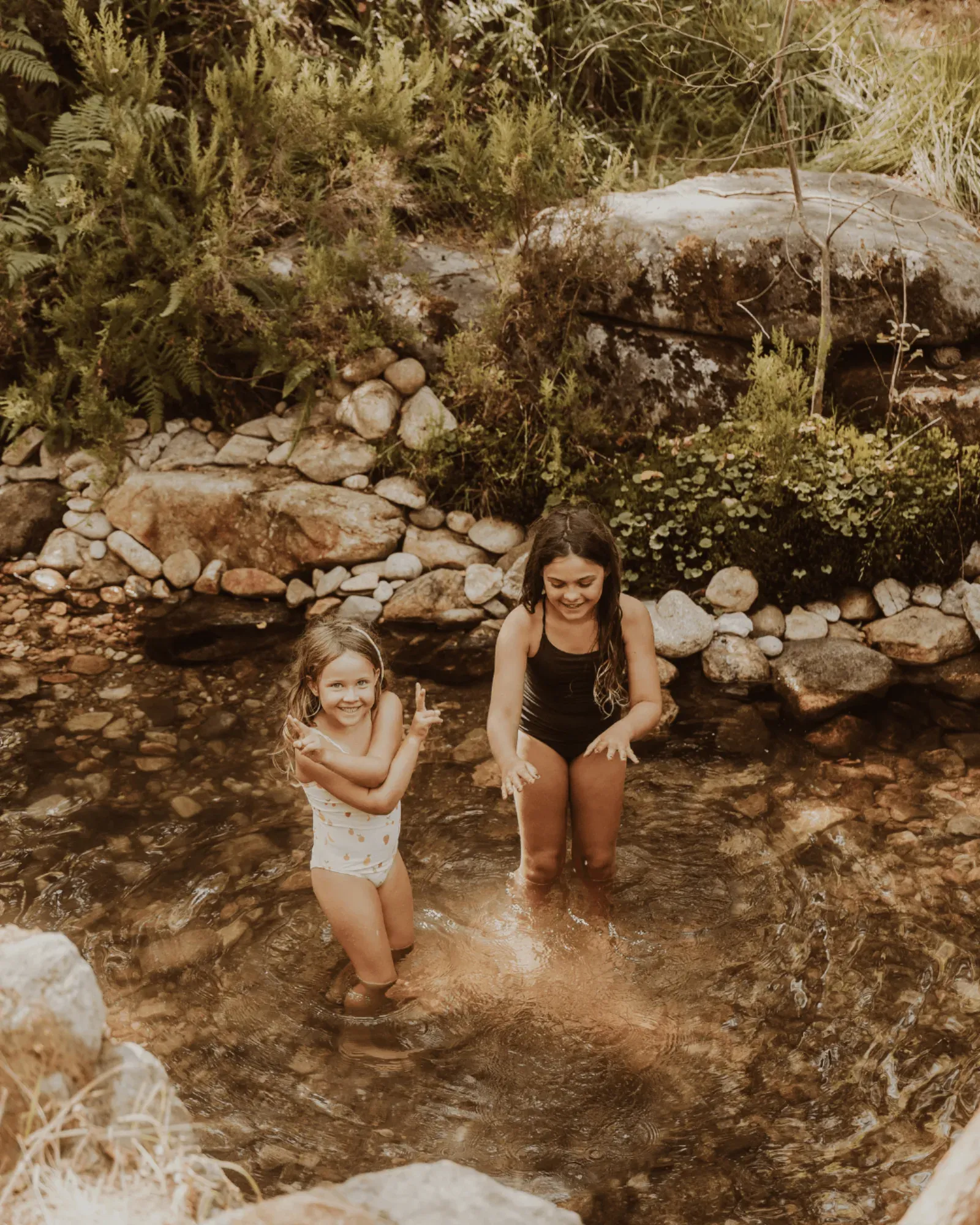 Mãe e criança a chapinhar numa poça entre rochas